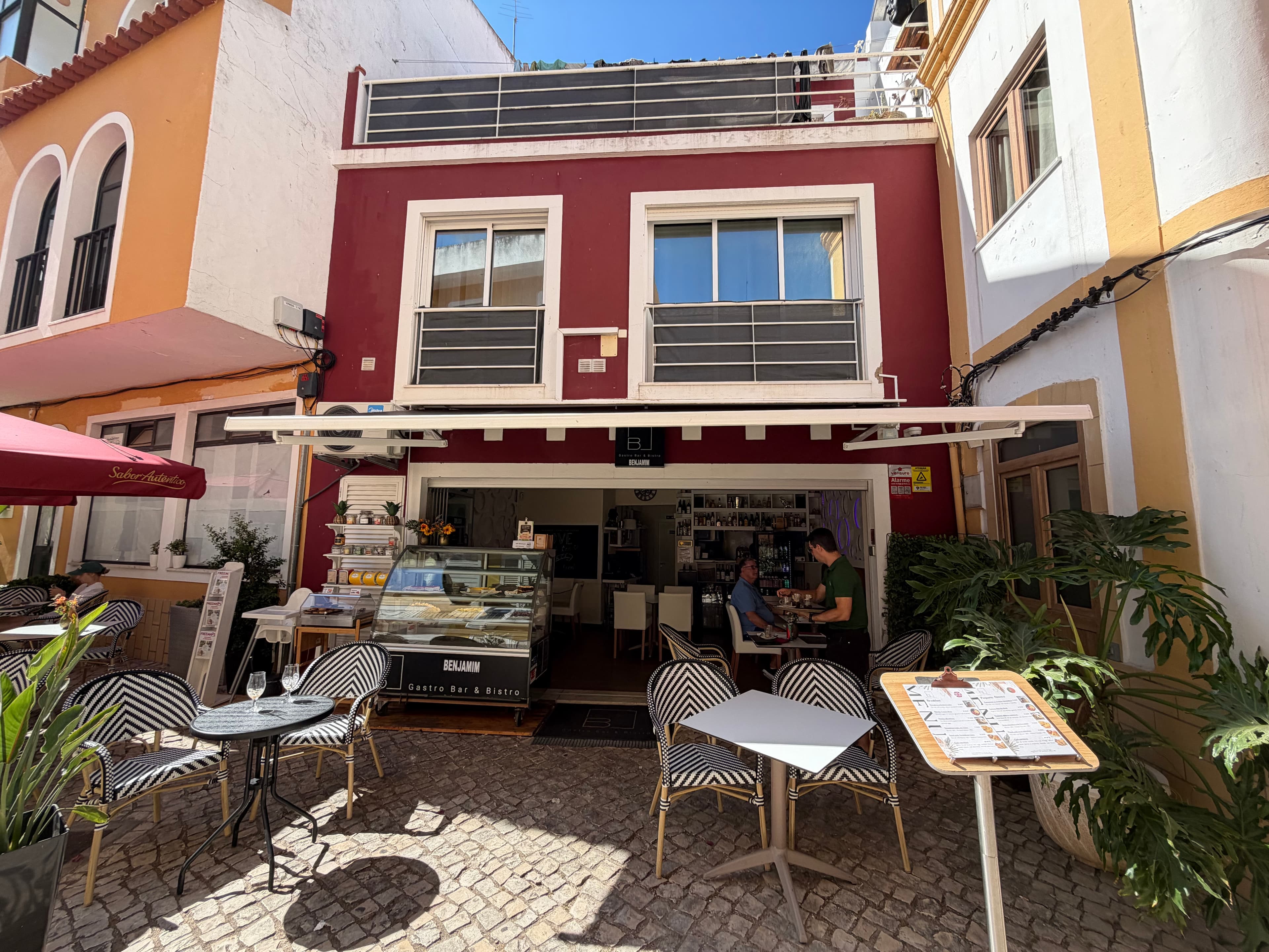 Benjamim Gastro Bar & Bistro on a sunny cobblestone street in Portugal, with black-and-white bistro chairs, a display case, a