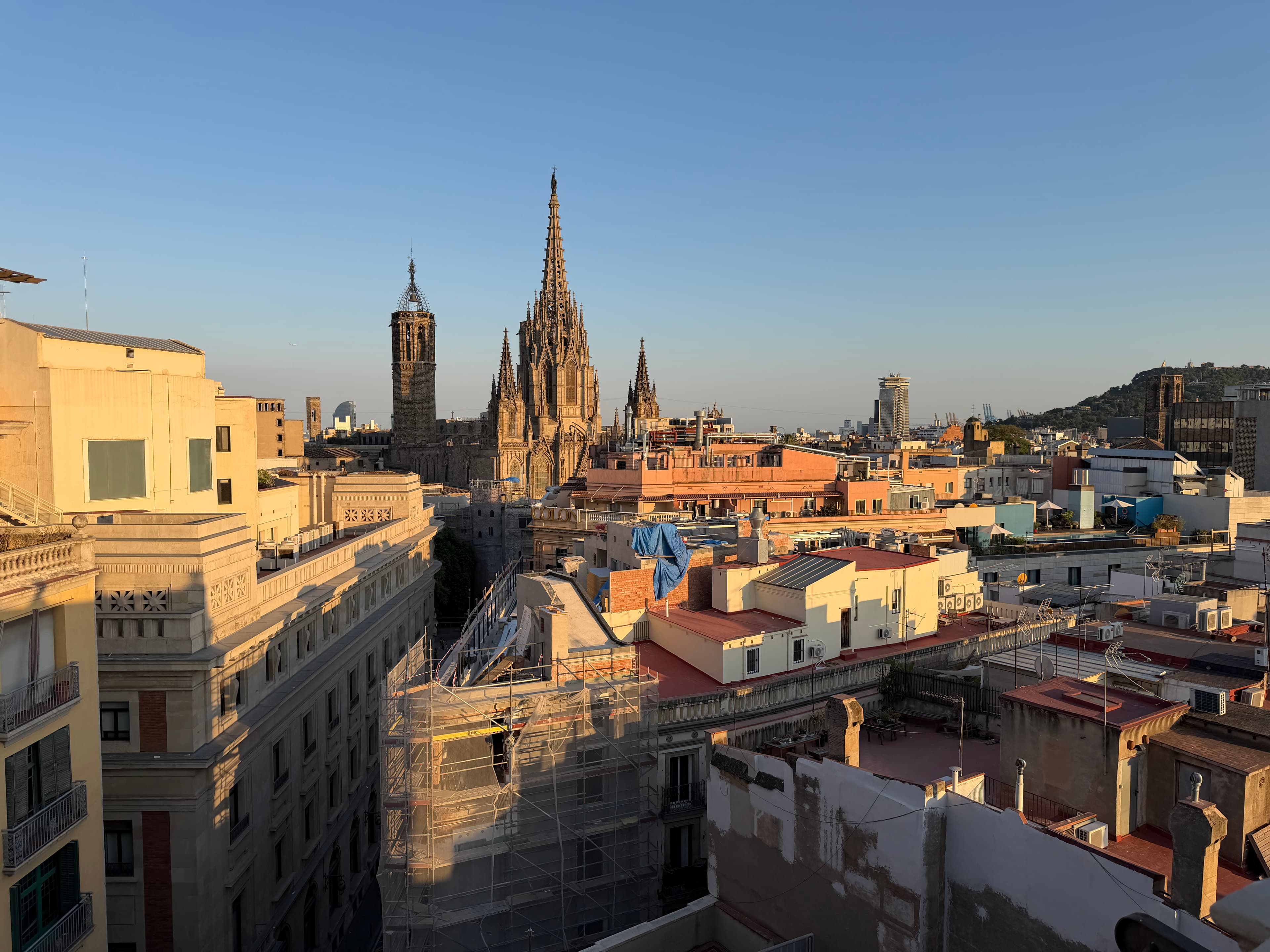 Barcelona rooftop panorama at golden hour with Gothic Cathedral spires rising above densely packed old city buildings under a