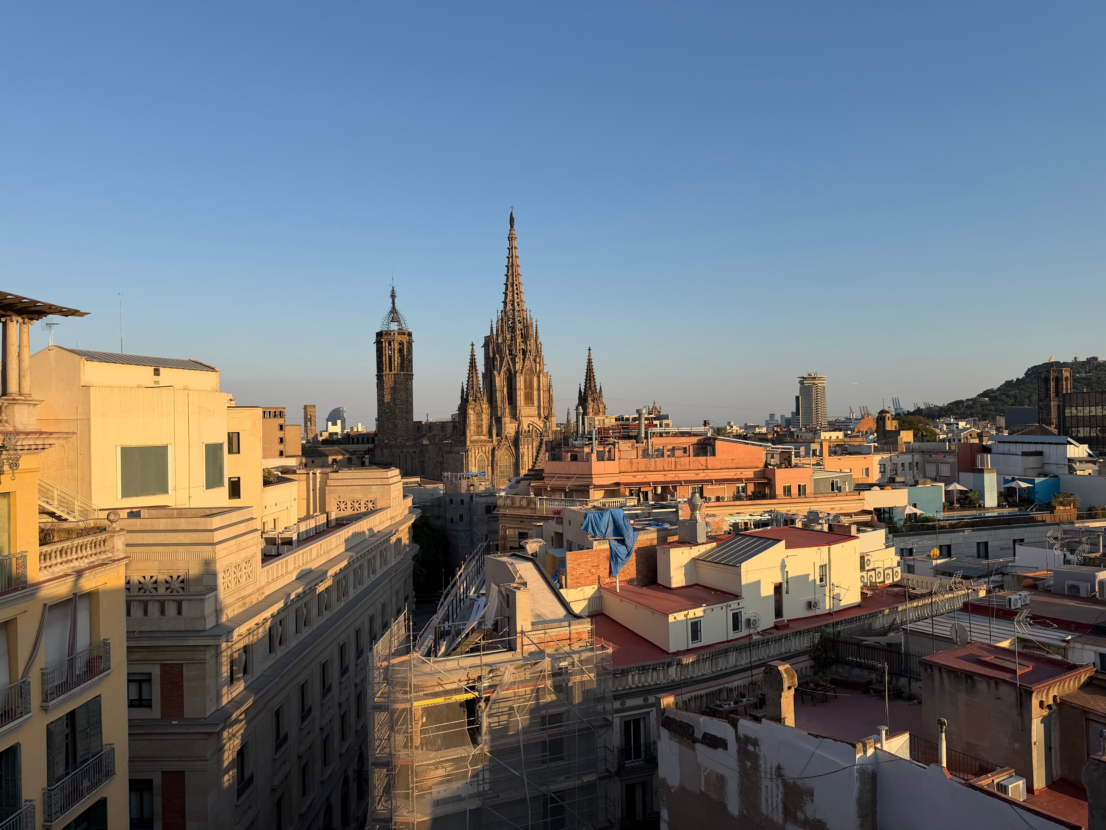 Rooftop panorama of Barcelona's Gothic Quarter at golden hour, with Barcelona Cathedral's spires rising above sun-warmed terr
