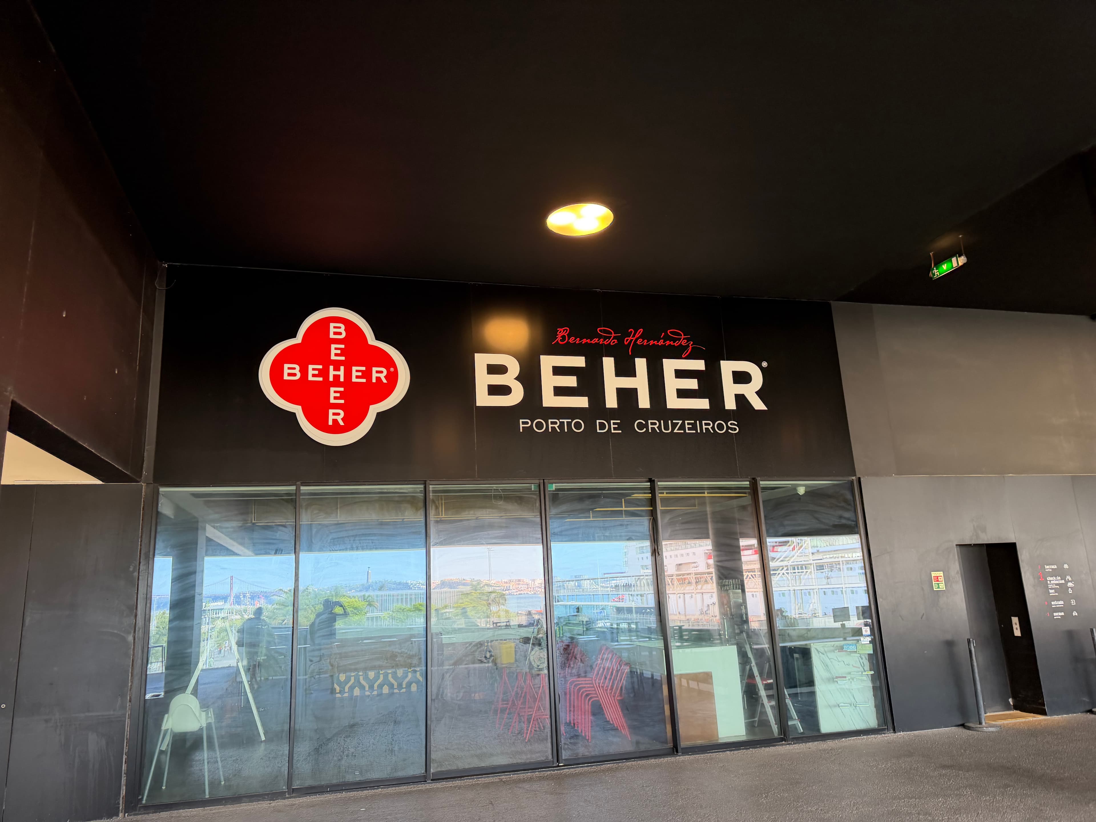 Beher Porto de Cruzeiros storefront with bold black signage and red logo, glass windows reflecting a cruise port and waterfro