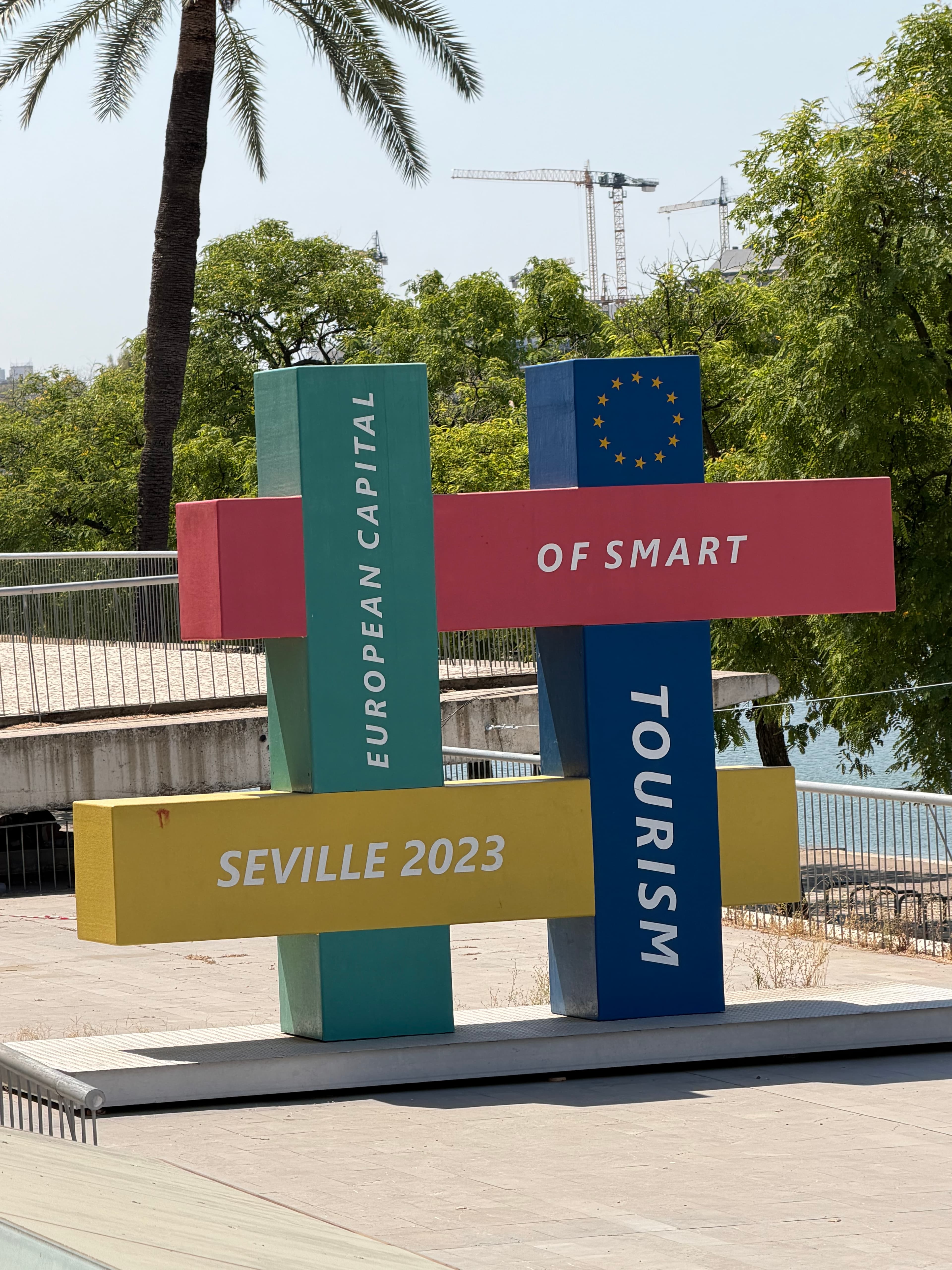 Colorful hashtag-shaped sculpture reading 'European Capital of Smart Tourism – Seville 2023' with EU stars, palm tree and riv