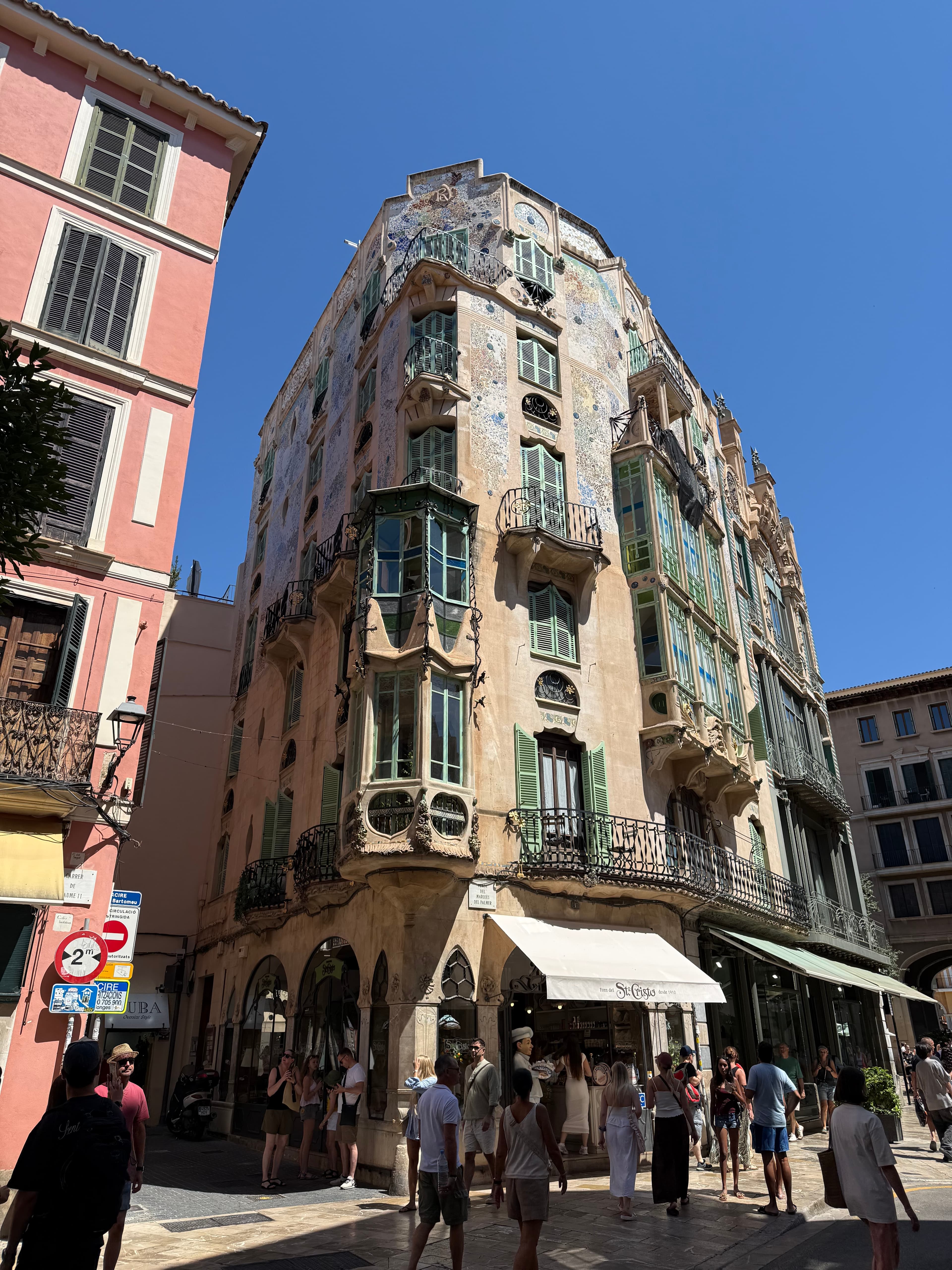 Ornate Modernista corner building with mosaic facade, wrought-iron balconies, and green shutters on a sunny Palma de Mallorca