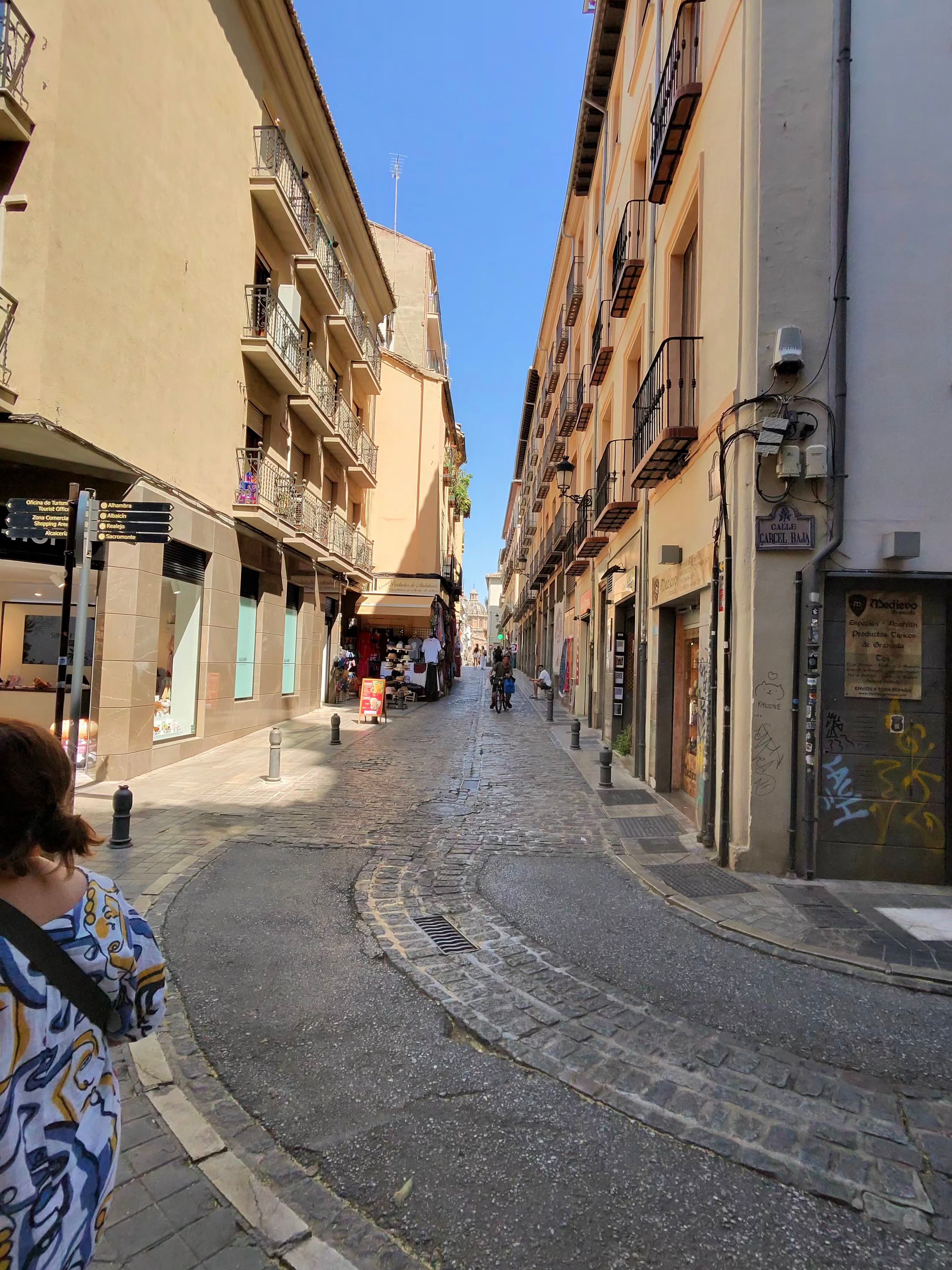 Narrow cobblestone street in Granada's old town on a sunny day, flanked by multi-story buildings with iron balconies and smal