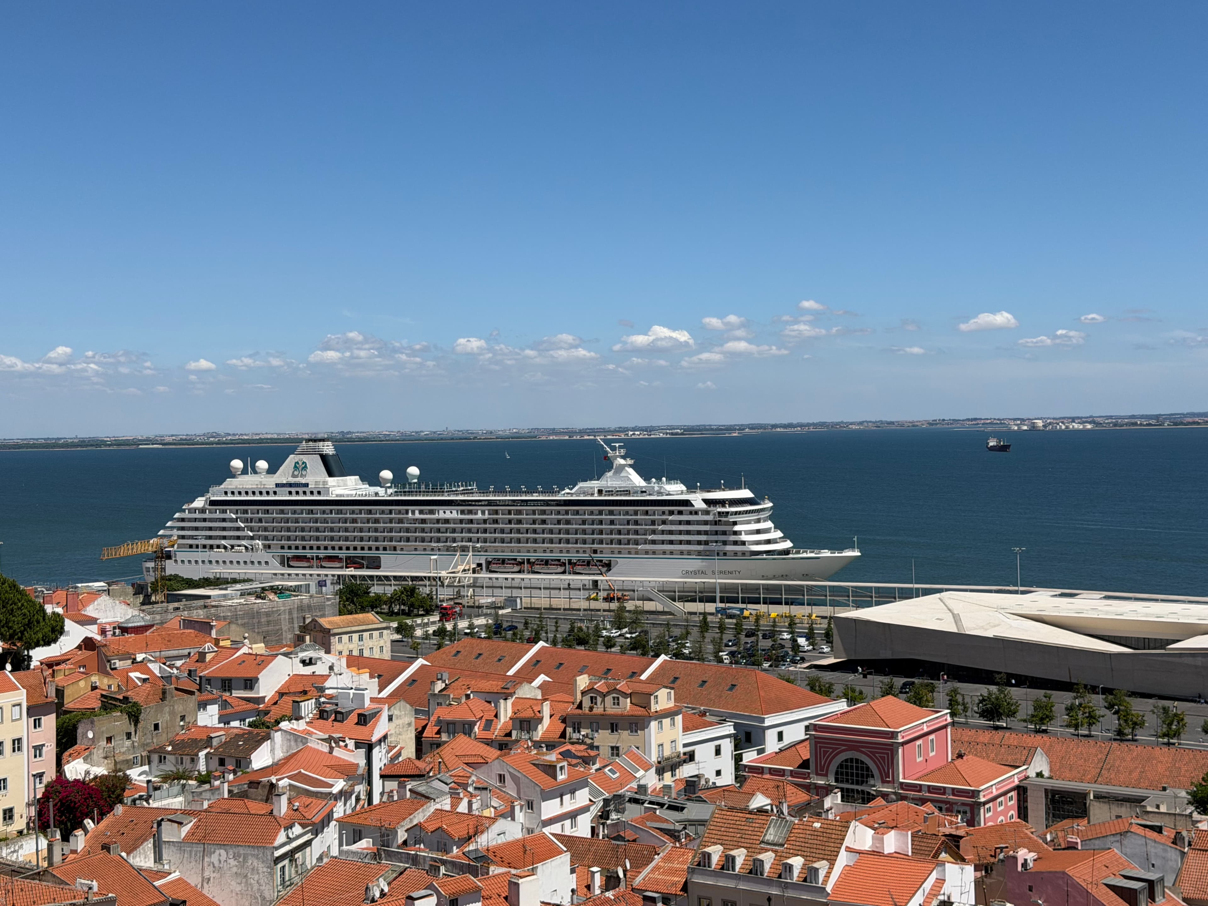 Aerial daytime view over Lisbon's terracotta rooftops with the Crystal Serenity cruise ship docked on the Tagus River under a